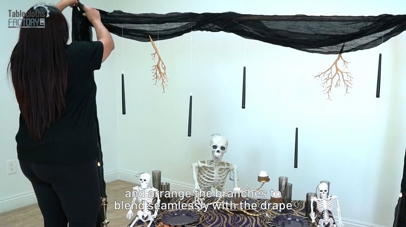 Draping black fabric and arranging gold branches for a haunting backdrop in a Halloween table setup.