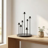 Modern black multi-arm candle holder on wooden table with potted plant.