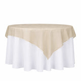 Round table with a beige tablecloth draped over a white tablecloth