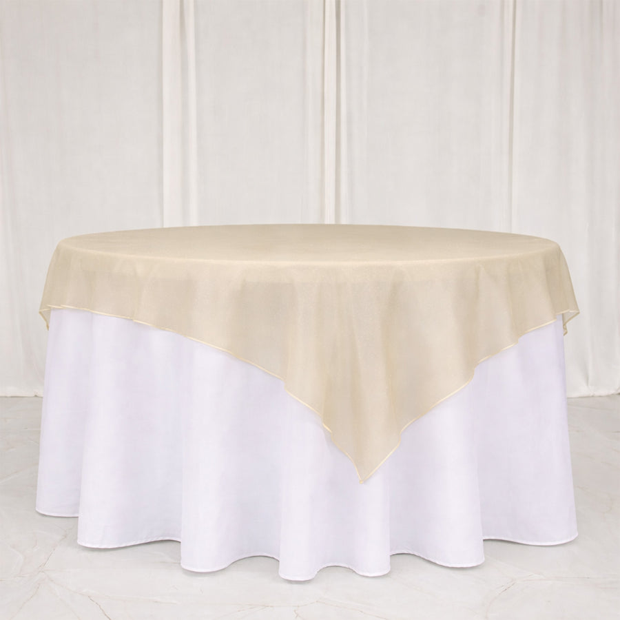 Round table with a beige overlay cloth on a white tablecloth.