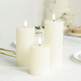 Three white pillar candles of varying heights on a table.