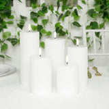 White pillar candles grouped on a table with greenery in the background.