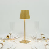 Gold table lamp with pleated shade, surrounded by elegant dinnerware.