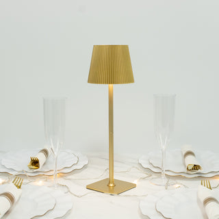 Gold table lamp with pleated shade, surrounded by elegant dinnerware.