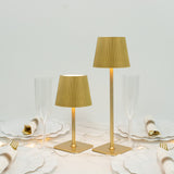 Gold table lamps with pleated shades on a dining table with elegant dinnerware.