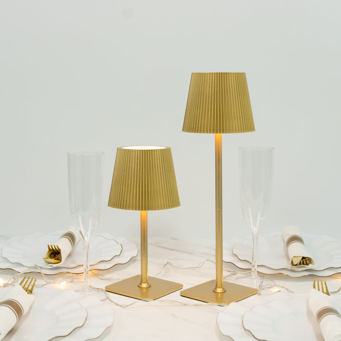 Gold table lamps with pleated shades on a dining table with elegant dinnerware.