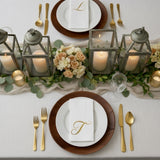Elegant table setting with gold utensils, lanterns, and floral centerpiece.