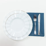 White plate with gold rim, fork, knife, and blue napkin on white background.