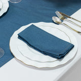 Blue napkin on a white plate set on a table with silver utensils.