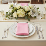 Elegant dining setup with pink napkin, fine china, and floral centerpiece.