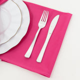 Silver fork and knife on a pink napkin with a white plate.