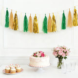 Party decor with tassel garland, cake, cupcakes, and flowers on a table.