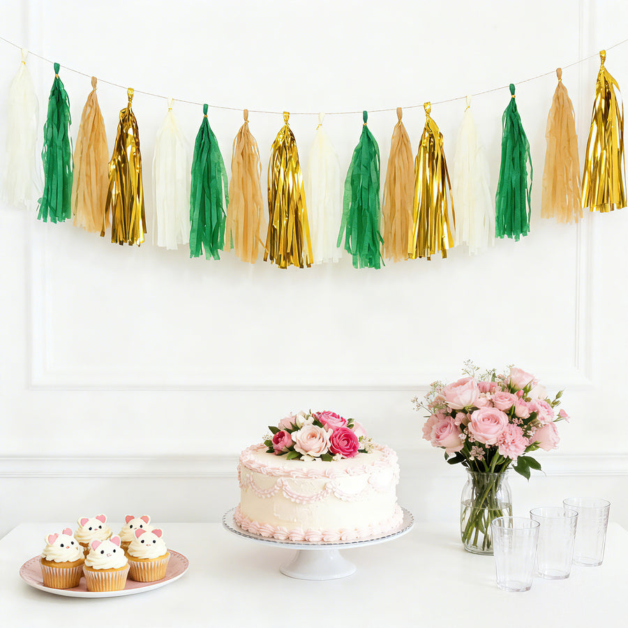 Party decor with tassel garland, cake, cupcakes, and flowers on a table.