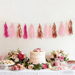Party decorations with pink and rose gold tassels, cake, and assorted sweets.