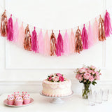 Birthday party decor with pink and gold tassel garland, cake, cupcakes, and flowers.