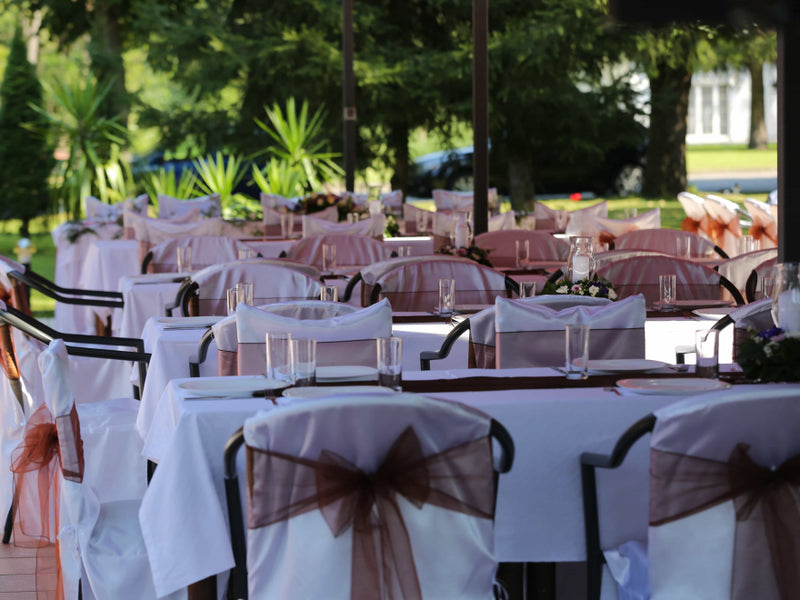 Outdoor wedding reception tables with white linens and brown chair sashes