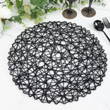 Black woven round placemat with intricate design on a marble table.