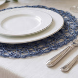 Elegant white dinner plates with blue woven placemat and silver cutlery
