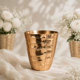 Gold hammered metal vase with white flowers on a soft beige backdrop