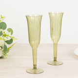 Green ribbed champagne flutes set on a wooden table with a floral arrangement.