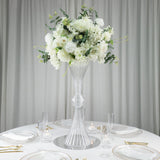 Elegant floral arrangement in a tall clear vase on a beautifully set dining table.