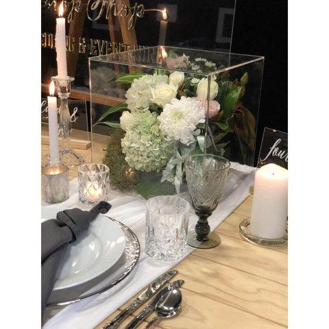 Acrylic box with floral arrangement beside a cake