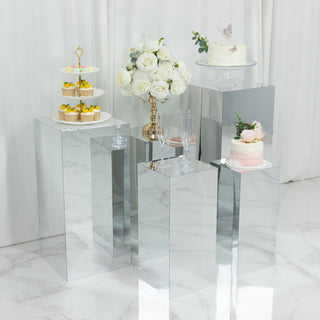 Mirrored display pedestals with cakes and floral arrangements for events.