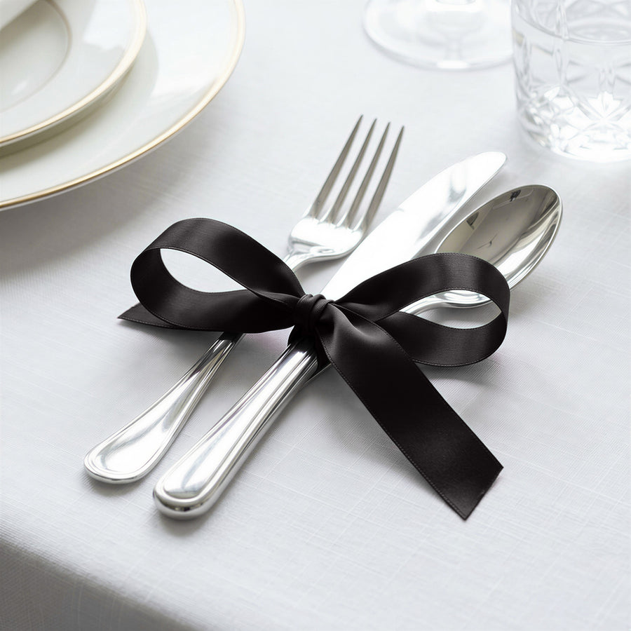 Elegant table setting with black ribbon tied around silver cutlery and utensils