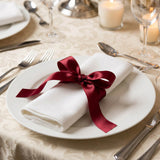 Elegant restaurant table setting with white napkin and burgundy ribbon bow