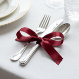 Elegant table setting with burgundy ribbon tied around silver cutlery