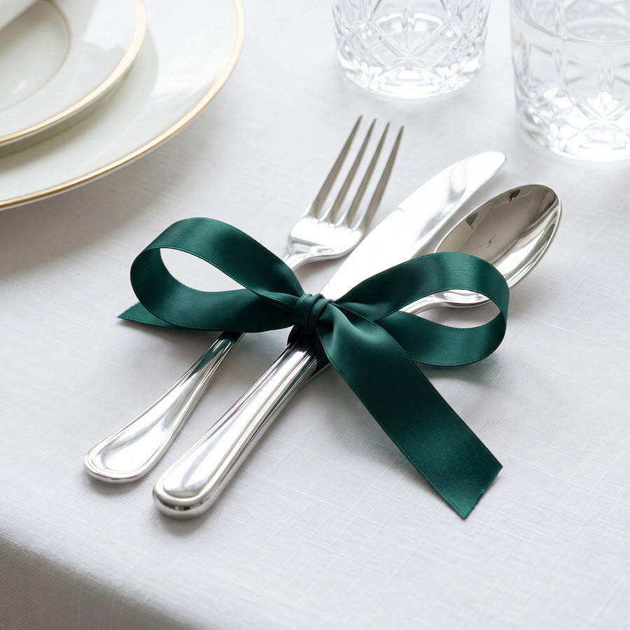 Elegant table setting with silver cutlery tied by a green ribbon on white tablecloth