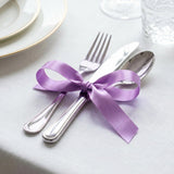 Purple ribbon tied around silver cutlery on a white table setting