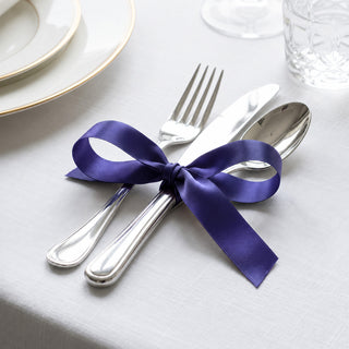 Purple ribbon tied around silver fork, knife, and spoon on a white table setting