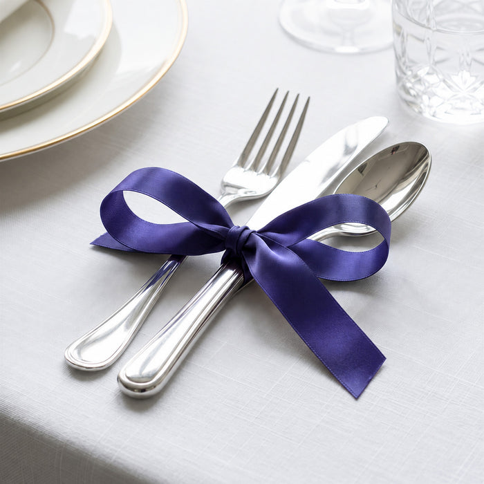 Purple ribbon tied around silver fork, knife, and spoon on a white table setting