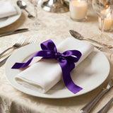 Elegant table setting with white napkin tied by purple ribbon on a dinner plate