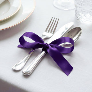 Elegant silver cutlery tied with purple ribbon on white table setting