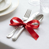 Elegant table setting with silverware tied with red ribbon on white cloth