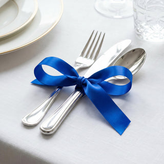 Blue ribbon tied around silver cutlery on a white table setting