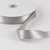 Silver satin ribbon spool with loose ribbon on white background