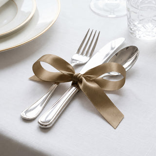 Elegant gold ribbon tied around silver cutlery on a white table setting