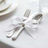 Elegant white ribbon tied around silver fork and spoon on a formal table setting