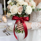 Bride holding ivory rose bouquet with burgundy ribbon at wedding reception