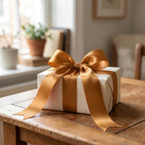 White gift box with gold ribbon bow on rustic wooden table