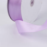 Lavender satin ribbon spool with ribbon unrolling on white background