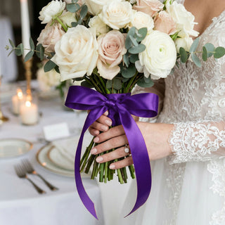 Bride holding white and blush rose bouquet with purple ribbon and lace dress