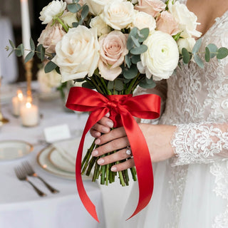 Bride holding white rose bouquet with red ribbon in lace wedding dress