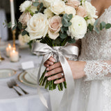 Bride holding white rose and eucalyptus wedding bouquet with silver ribbon