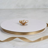 White round cake board with gold ribbon and decorative bow centerpiece