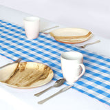 Table setting with plates, mugs, and utensils on a blue checkered tablecloth