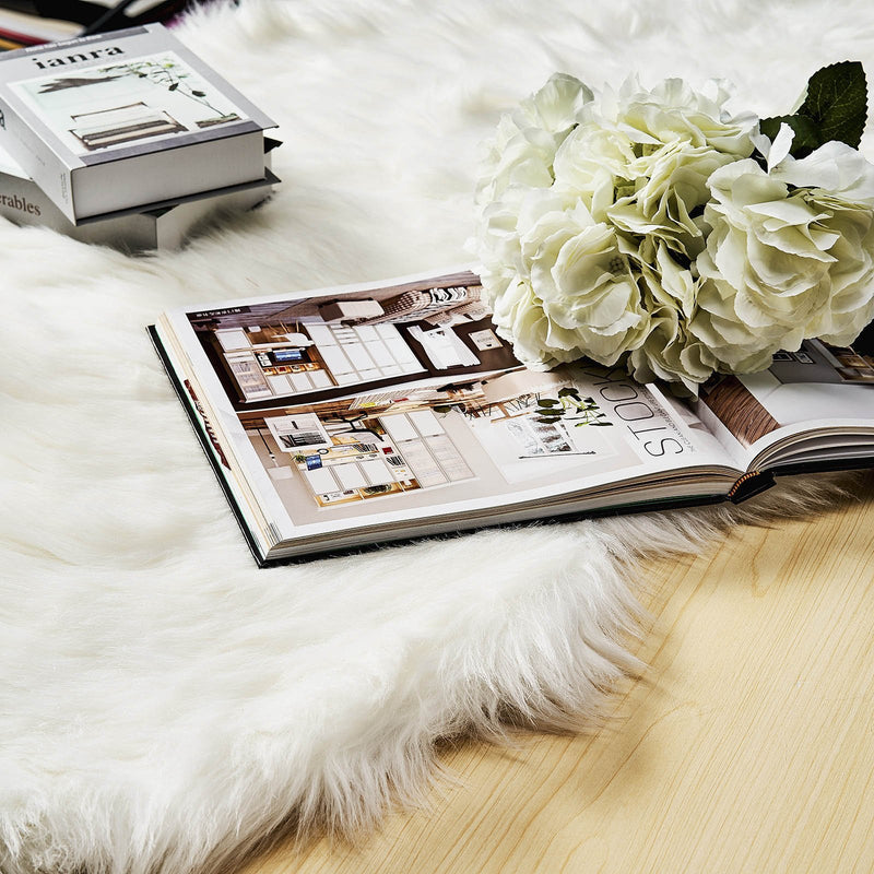 White sheepskin rug under a book and flowers on a table